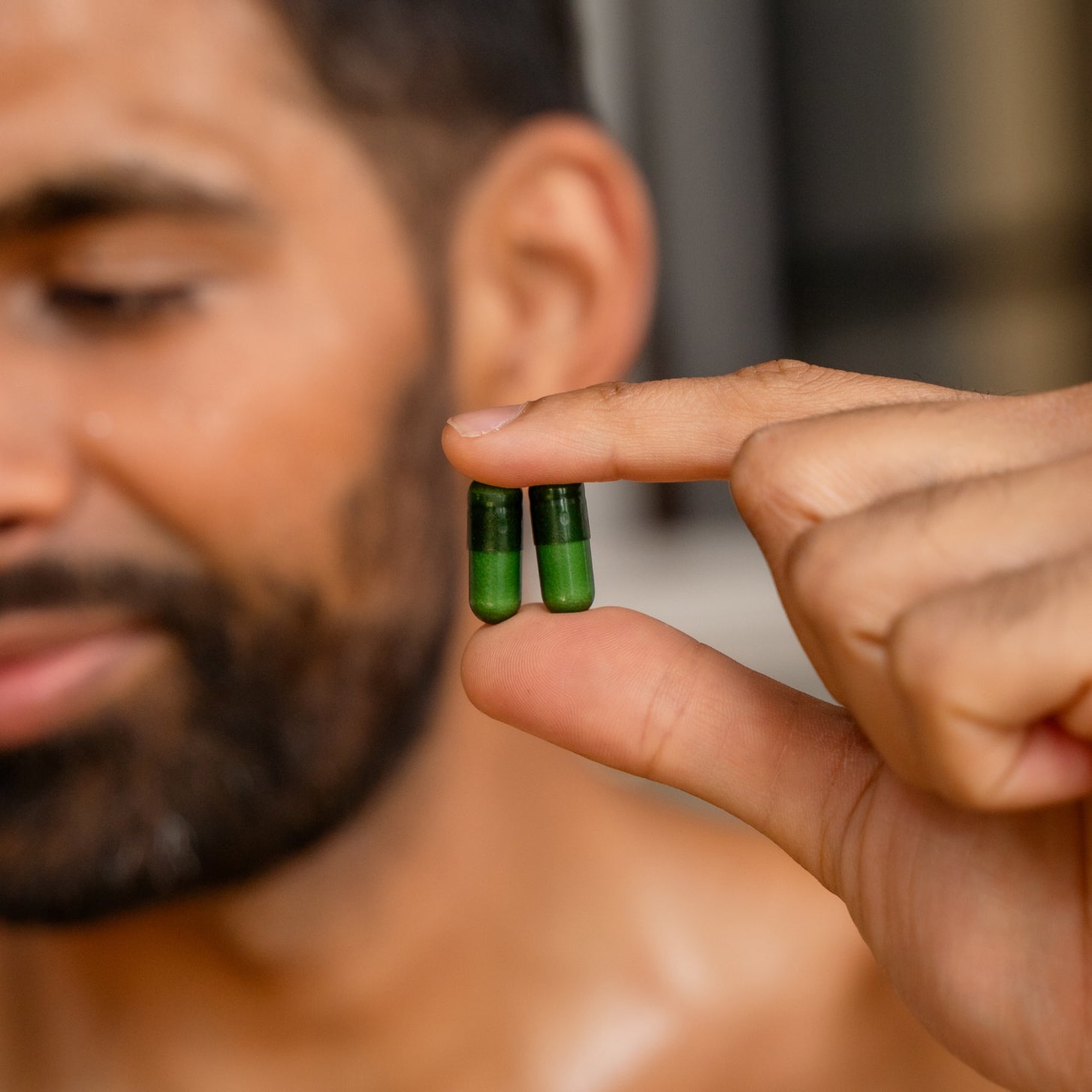 Man holding two green capsules close to his face