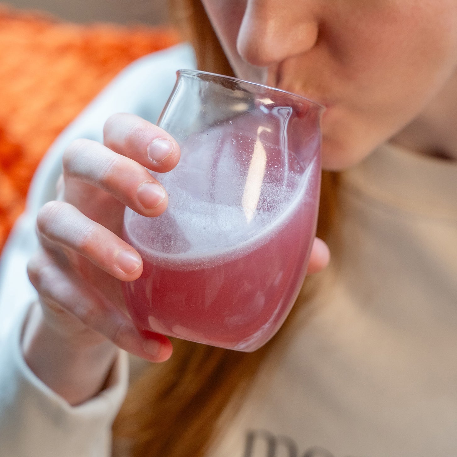 Woman drinking from a glass of pink vegan collagen drink.